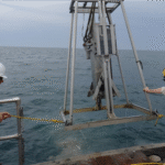 photo of two man on boat pulling in large metal device on crane