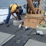 photo of many on boat bending over and working on scientific instrument